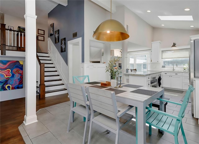 dining room featuring a skylight, stairs, decorative columns, high vaulted ceiling, and light wood-style floors