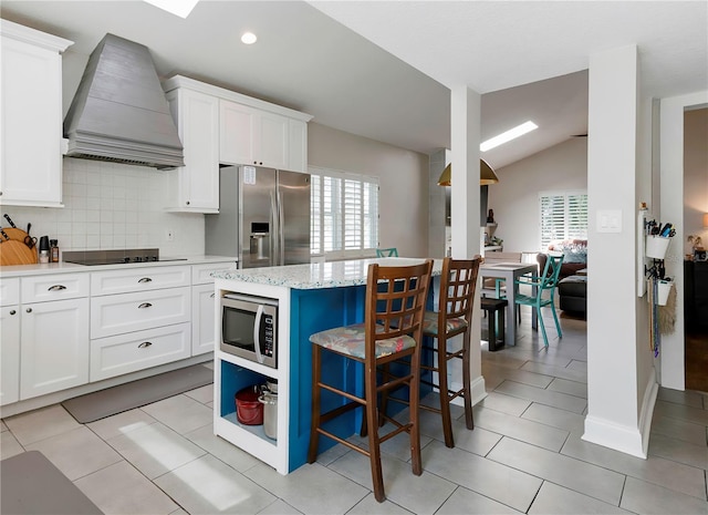 kitchen featuring a kitchen bar, stainless steel appliances, white cabinetry, lofted ceiling, and custom range hood