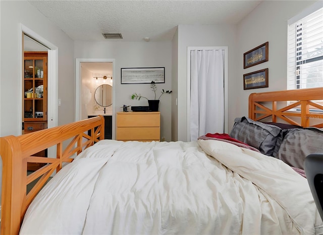 bedroom with a textured ceiling, visible vents, and ensuite bathroom