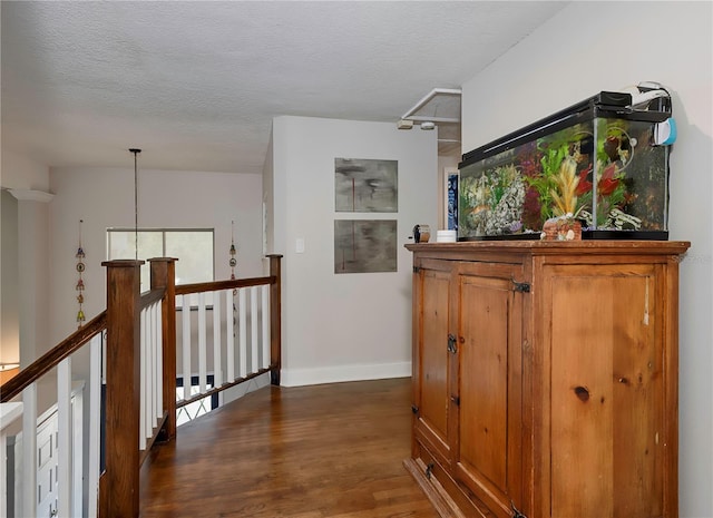 hall featuring a textured ceiling, an upstairs landing, baseboards, and dark wood-style floors