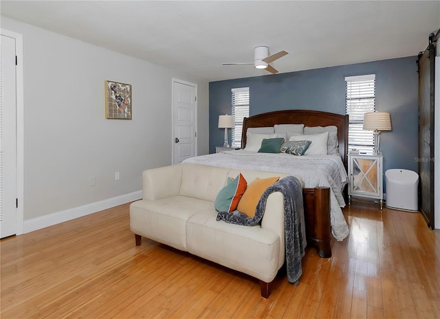 bedroom with a barn door, baseboards, ceiling fan, and hardwood / wood-style flooring