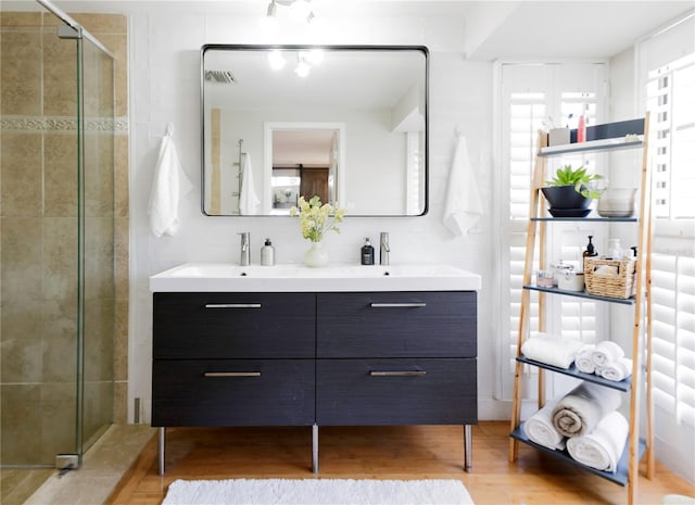 full bathroom with double vanity, wood finished floors, a sink, visible vents, and a shower stall