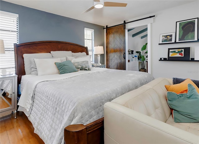 bedroom with ceiling fan, a barn door, and wood-type flooring