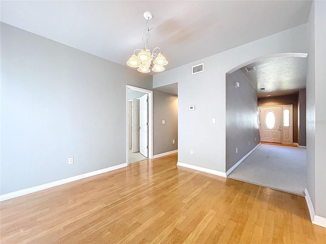 spare room with a chandelier, visible vents, light wood-style flooring, baseboards, and arched walkways