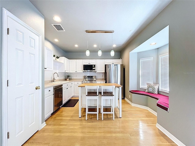 kitchen featuring stainless steel appliances, white cabinets, a center island, a sink, and visible vents