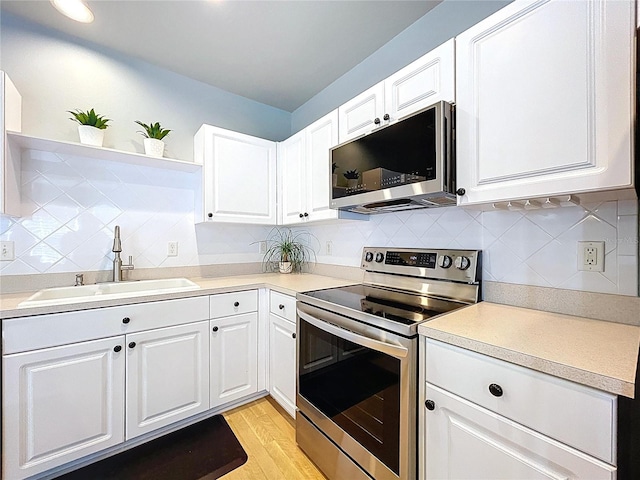 kitchen with decorative backsplash, appliances with stainless steel finishes, light countertops, white cabinets, and a sink