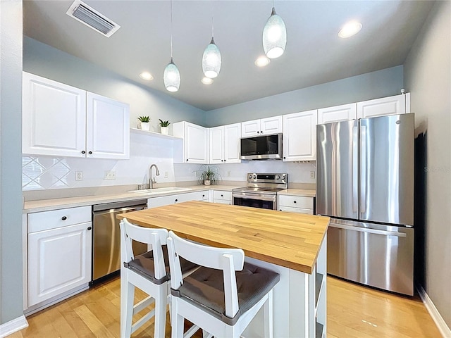 kitchen featuring a sink, stainless steel appliances, light wood-style floors, visible vents, and white cabinetry