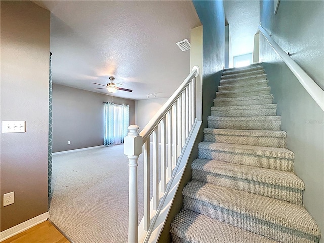 stairway with ceiling fan, visible vents, and baseboards