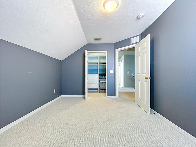 additional living space with a textured ceiling, visible vents, light colored carpet, and vaulted ceiling