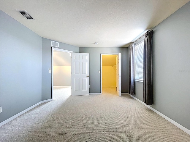 unfurnished bedroom with visible vents, a spacious closet, light colored carpet, and baseboards
