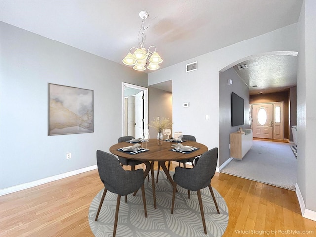 dining area featuring visible vents, a chandelier, baseboards, arched walkways, and light wood-type flooring