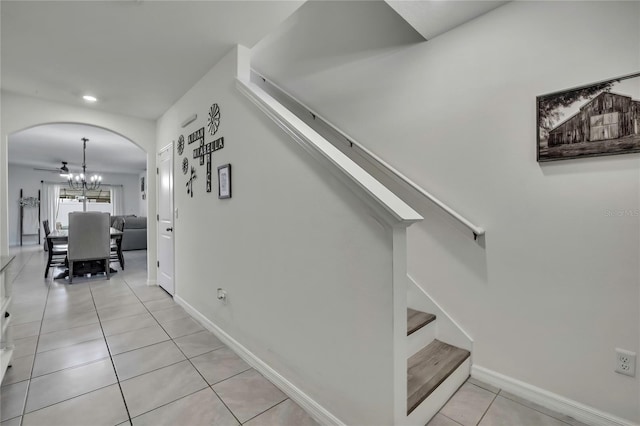 staircase with arched walkways, an inviting chandelier, baseboards, and tile patterned flooring