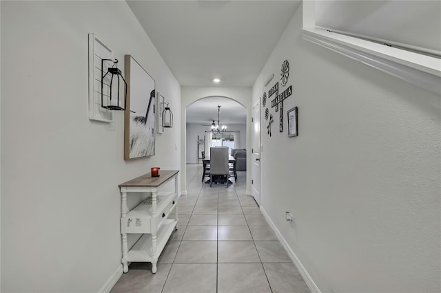 hall featuring arched walkways, light tile patterned floors, a notable chandelier, and baseboards