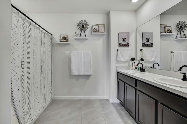 full bath with tile patterned floors, double vanity, baseboards, and a sink