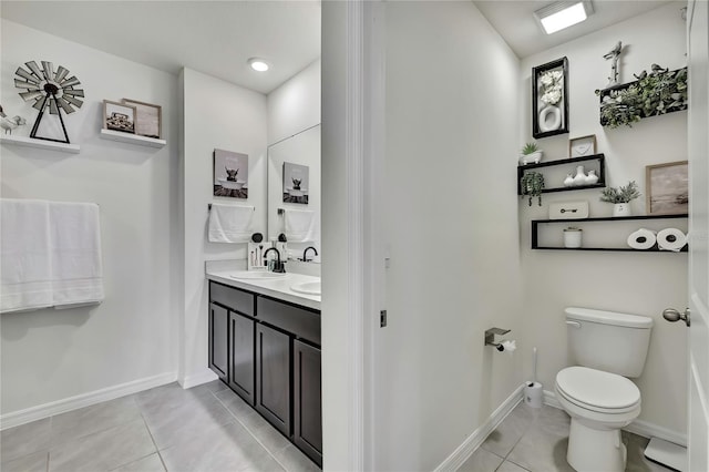 bathroom featuring baseboards, a sink, toilet, double vanity, and tile patterned floors