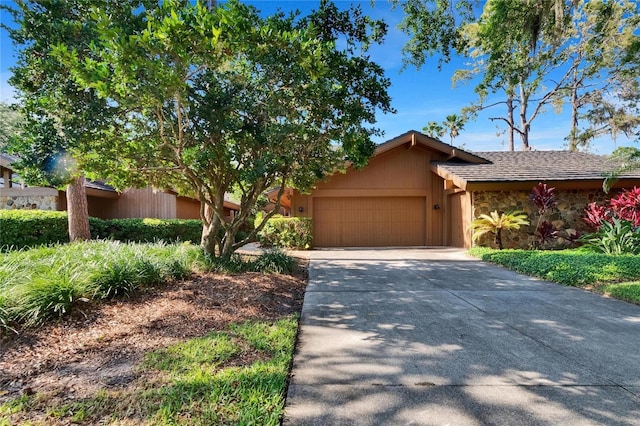 mid-century home featuring a garage, driveway, and stone siding