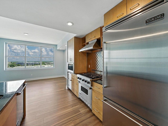 1208 E Kennedy Blvd Unit 1125, Tampa, FL 33602 - kitchen featuring premium appliances, extractor fan, brown cabinetry, dark wood-type flooring, and backsplash