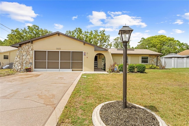 view of front of house featuring driveway, a front yard, a garage, fence, and stone siding