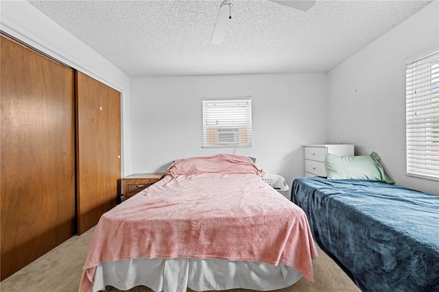 bedroom featuring ceiling fan, light carpet, a closet, and a textured ceiling