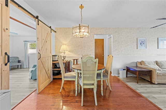 dining room featuring a textured ceiling, wallpapered walls, a barn door, and light wood finished floors