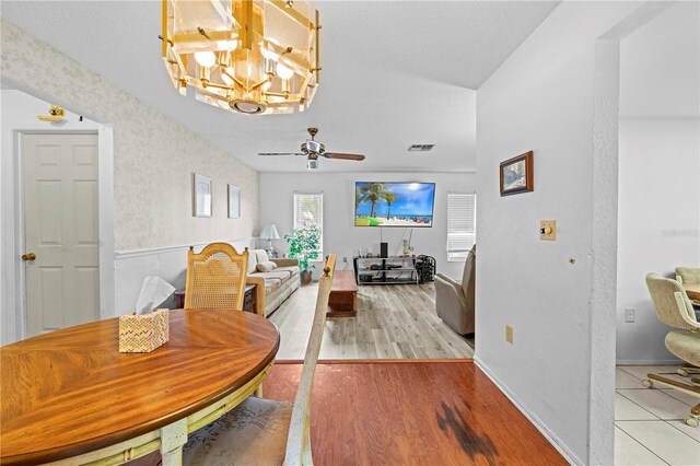 dining space with baseboards, visible vents, wood finished floors, and ceiling fan with notable chandelier
