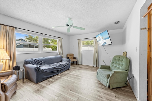 living area featuring ceiling fan, light wood-style flooring, a textured ceiling, and visible vents