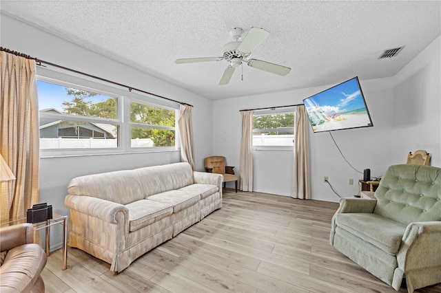 living area with a textured ceiling, visible vents, ceiling fan, and light wood finished floors