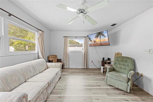 living area featuring visible vents, a textured ceiling, light wood finished floors, and ceiling fan