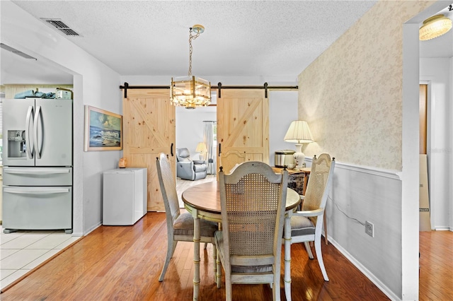 dining space featuring a textured ceiling, visible vents, a barn door, and wood finished floors