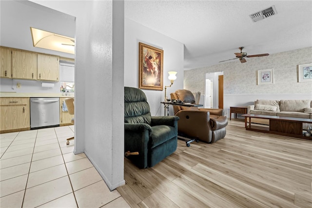 living area featuring ceiling fan, light wood finished floors, a textured ceiling, baseboards, and visible vents
