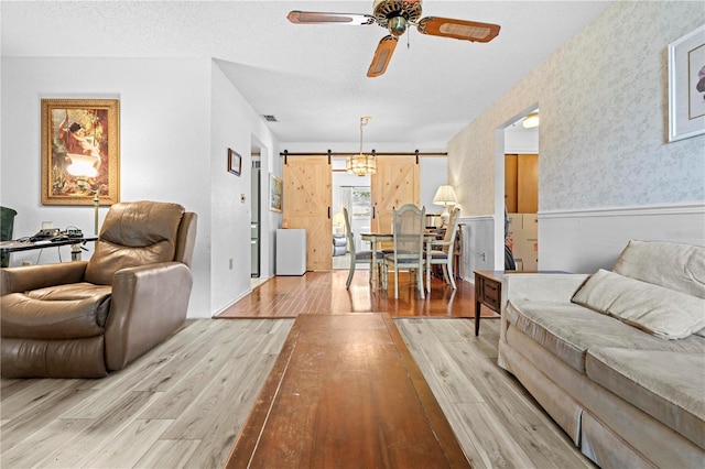 living room featuring ceiling fan, a barn door, a wainscoted wall, wood finished floors, and visible vents