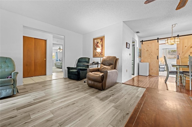 living area featuring a barn door, a textured ceiling, a ceiling fan, light wood-type flooring, and visible vents