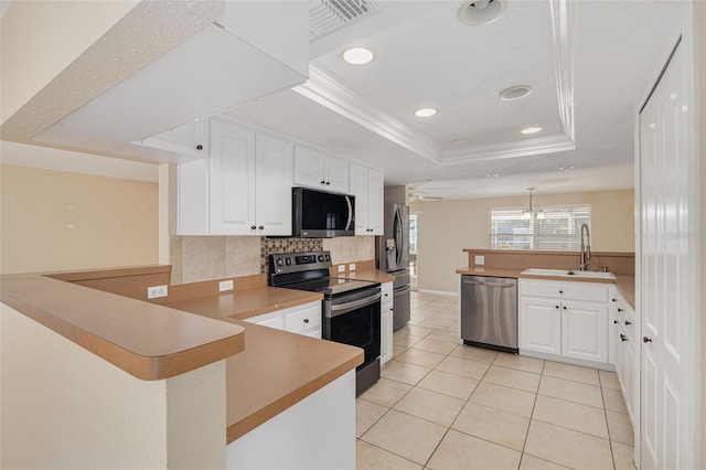 kitchen with a raised ceiling, a sink, a peninsula, stainless steel appliances, and backsplash