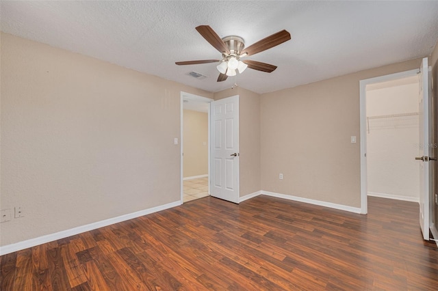 empty room featuring dark wood-style flooring, baseboards, a textured ceiling, visible vents, and ceiling fan