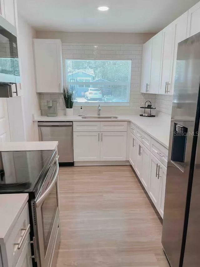 7101 N 9th St, Tampa, FL 33604 - kitchen featuring stainless steel appliances, a sink, tasteful backsplash, light wood finished floors, and white cabinets