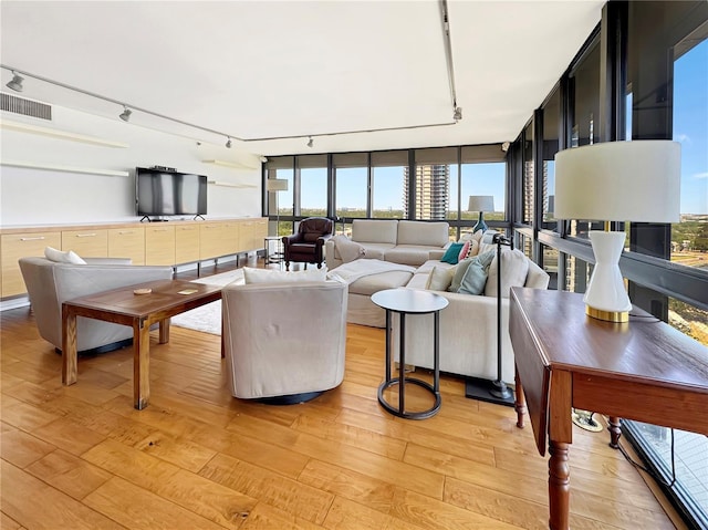 living area featuring rail lighting, a healthy amount of sunlight, visible vents, and light wood-type flooring