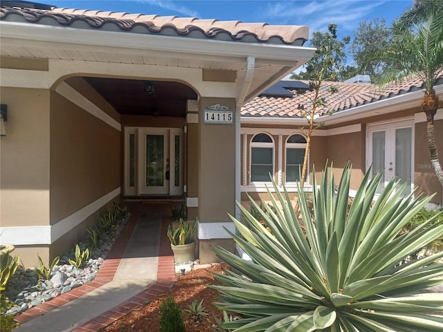 property entrance with stucco siding, a tiled roof, and french doors
