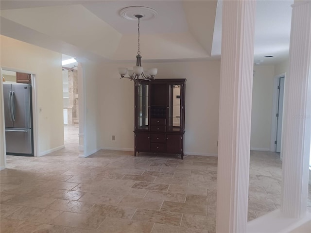 unfurnished dining area featuring stone tile floors, baseboards, an inviting chandelier, and a raised ceiling