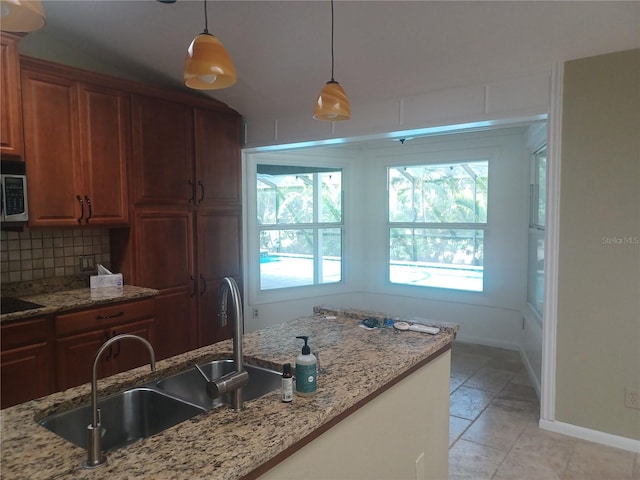 kitchen with a sink, stainless steel microwave, decorative light fixtures, baseboards, and decorative backsplash