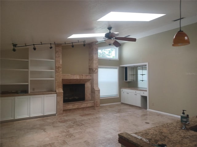 unfurnished living room with baseboards, a skylight, ceiling fan, track lighting, and a fireplace