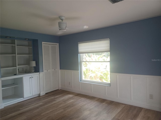 interior space with wainscoting, visible vents, a ceiling fan, wood finished floors, and a decorative wall