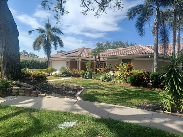 mediterranean / spanish-style house featuring a tile roof, a garage, roof mounted solar panels, a front yard, and stucco siding