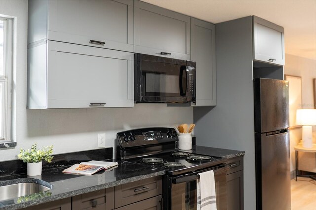 kitchen featuring a sink, gray cabinets, black appliances, and dark stone countertops