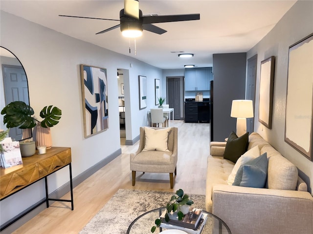 living area featuring light wood-type flooring, a ceiling fan, and baseboards