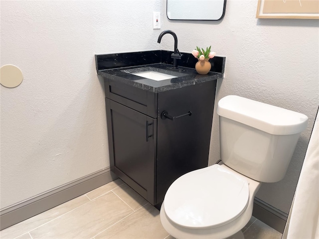 bathroom with toilet, vanity, a textured wall, and baseboards