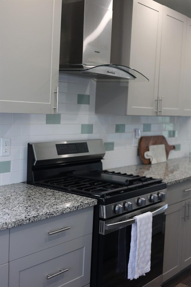 5973 Terrace Park Dr N Unit 311, Saint Petersburg, FL 33709 - kitchen featuring tasteful backsplash, light stone counters, gray cabinetry, wall chimney exhaust hood, and stainless steel range with gas cooktop