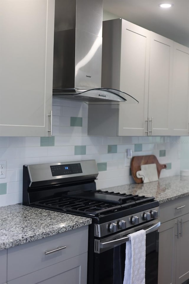 5973 Terrace Park Dr N Unit 311, Saint Petersburg, FL 33709 - kitchen with light stone counters, decorative backsplash, wall chimney exhaust hood, and stainless steel gas range oven