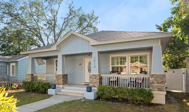 1410 25th St N, Saint Petersburg, FL 33713 - view of front facade with board and batten siding, stone siding, covered porch, and fence