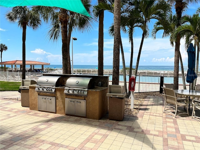 view of patio with exterior kitchen, a water view, a grill, and fence