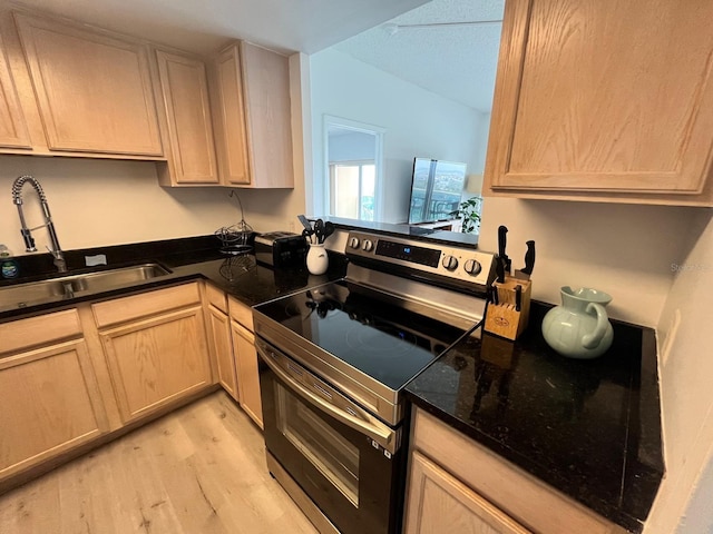 kitchen featuring electric range, light wood-type flooring, light brown cabinetry, dark stone countertops, and a sink